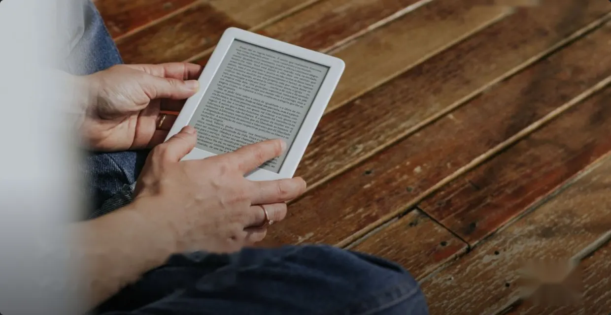 Hands holding an e-reader on a wooden floor