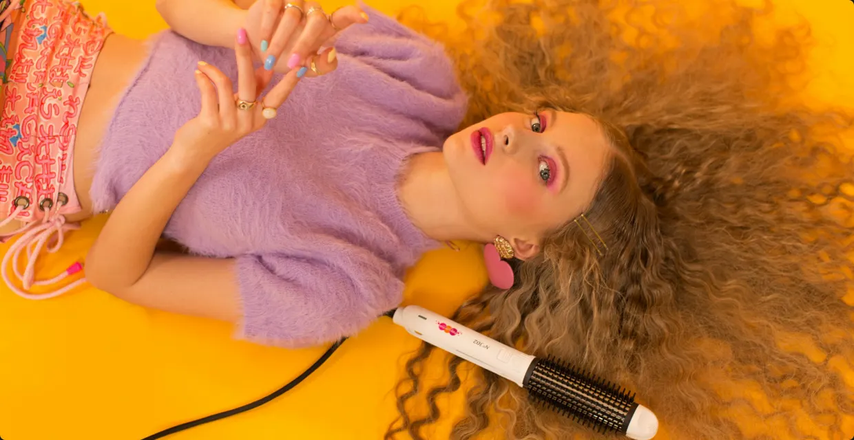 Woman with long curly hair holding a heated styling brush