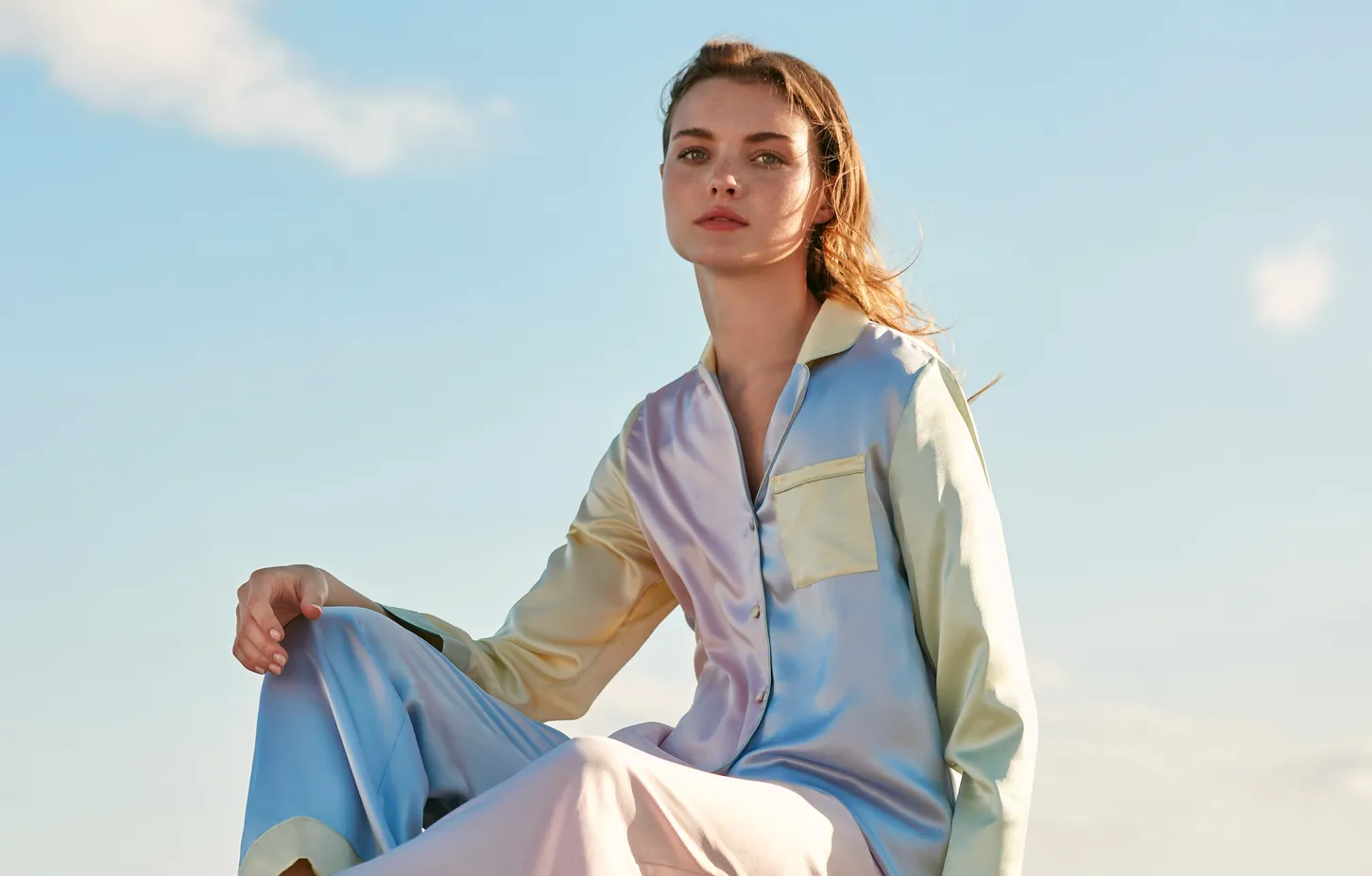 Frau in einem pastellfarbenen Seiden-Pyjama vor blauem Himmel