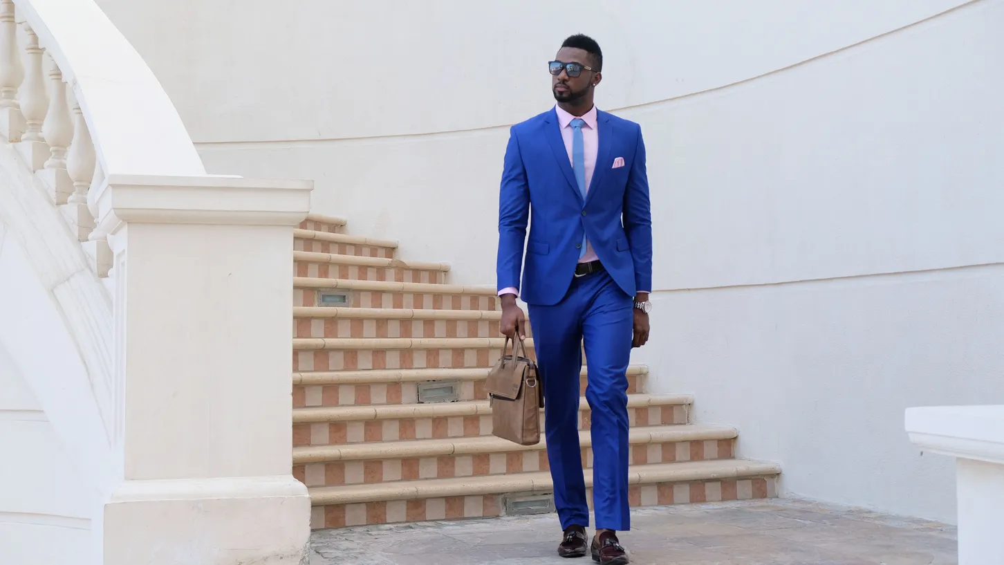 Man in a bright blue suit and sunglasses walking past a white staircase