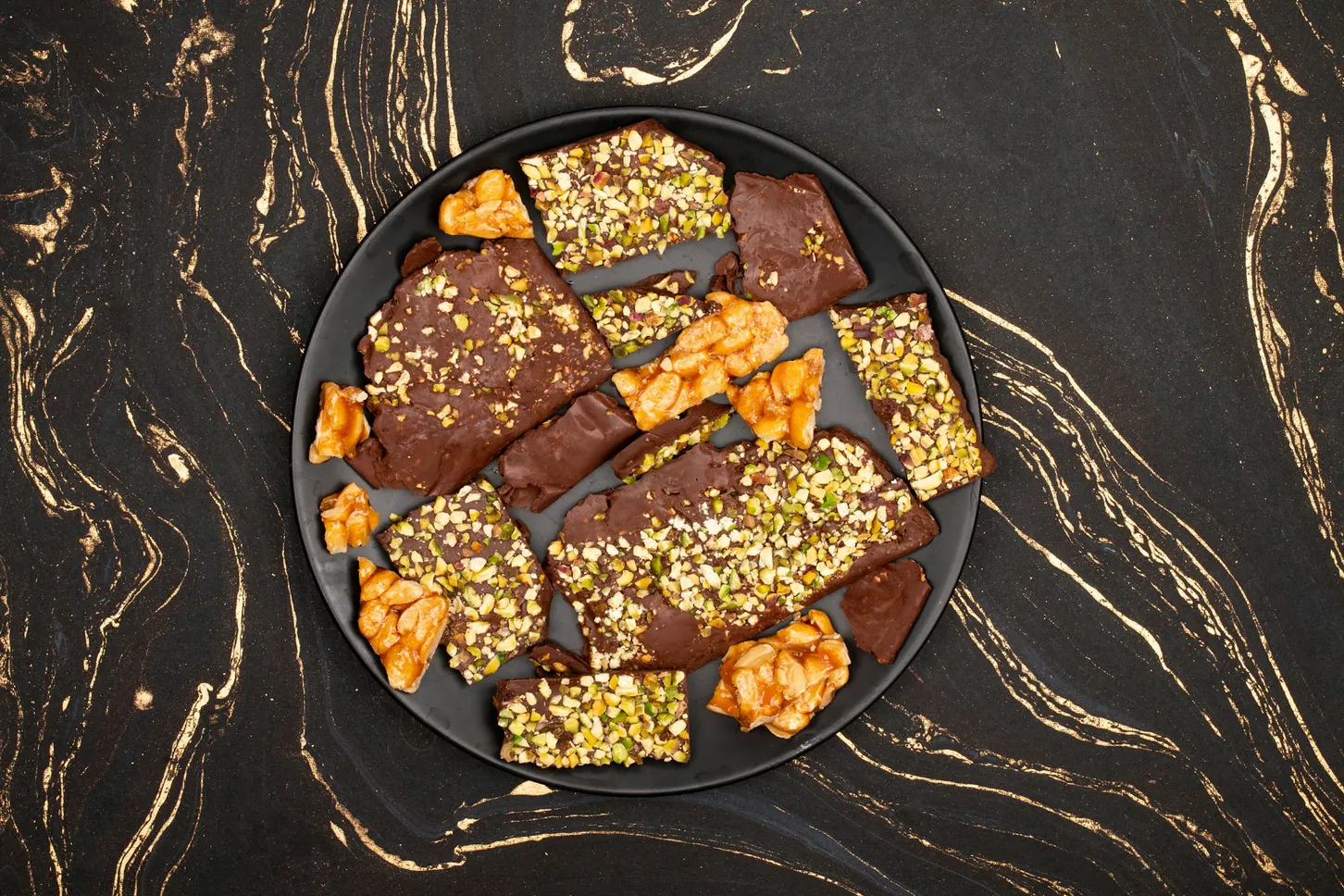 Chocolate bark with pistachios and nuts on a dark marble plate