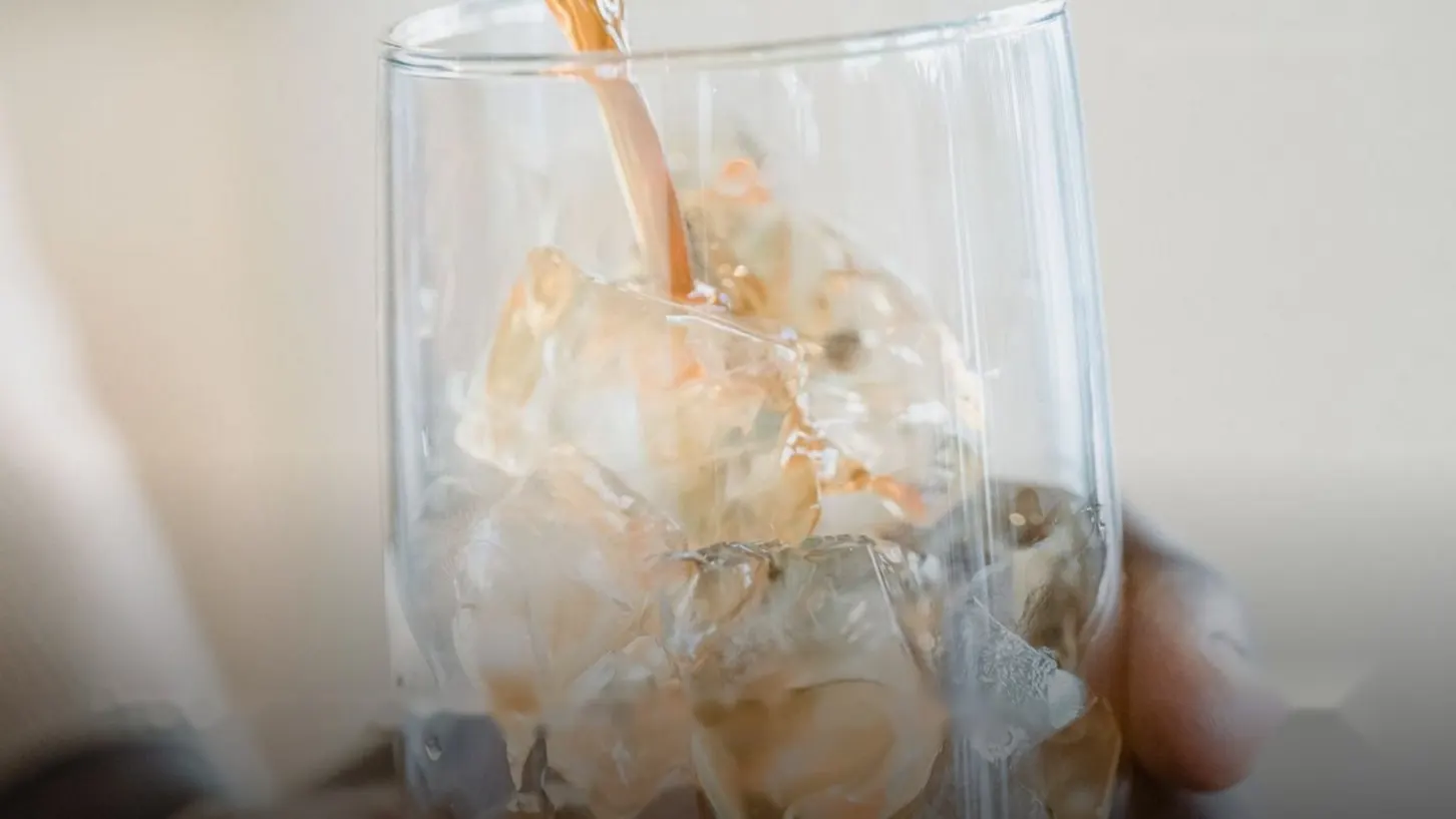 Iced coffee being poured into a glass full of ice