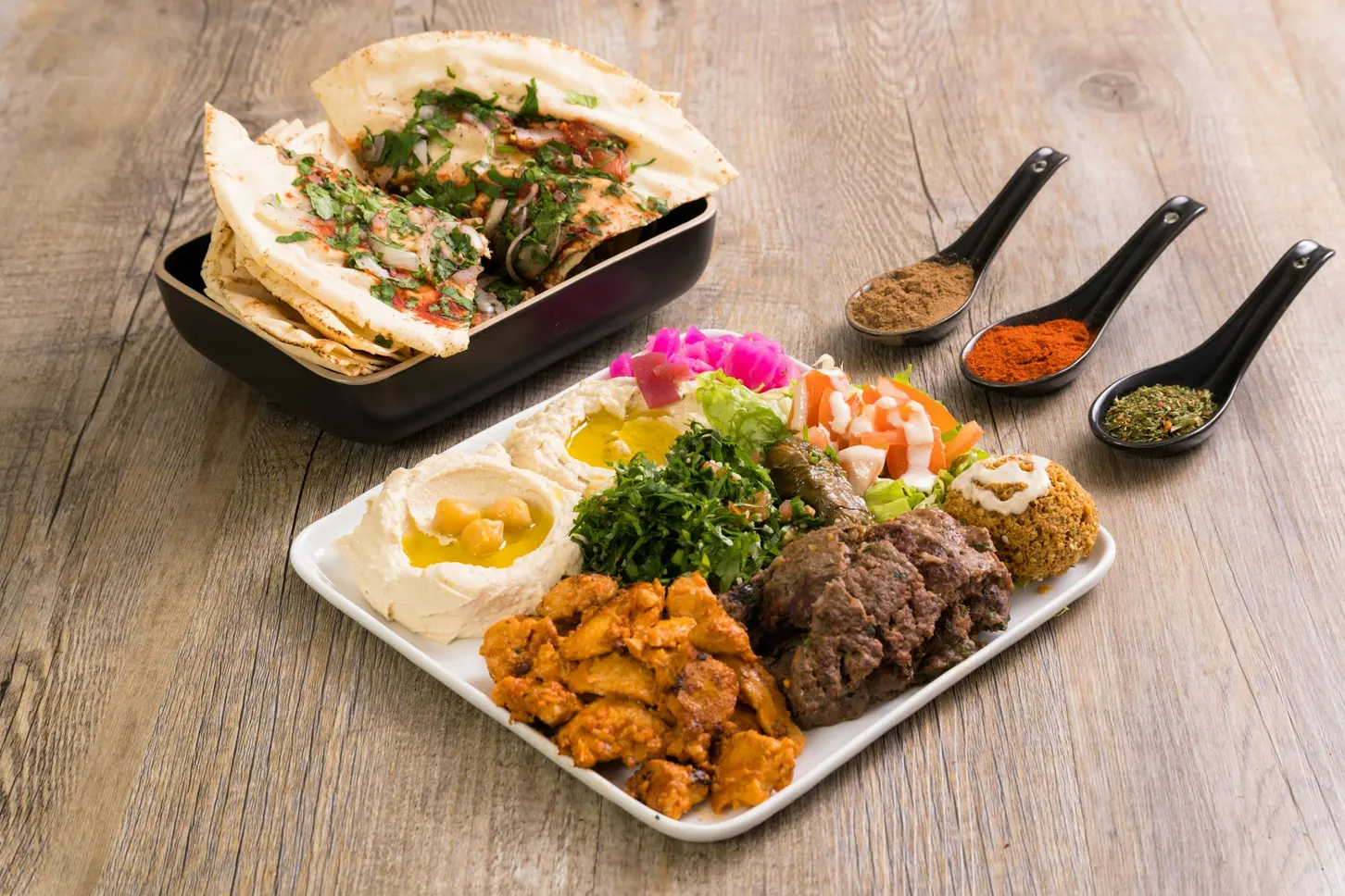 Mezze plate with hummus, salad and grilled meat next to spoons of spices